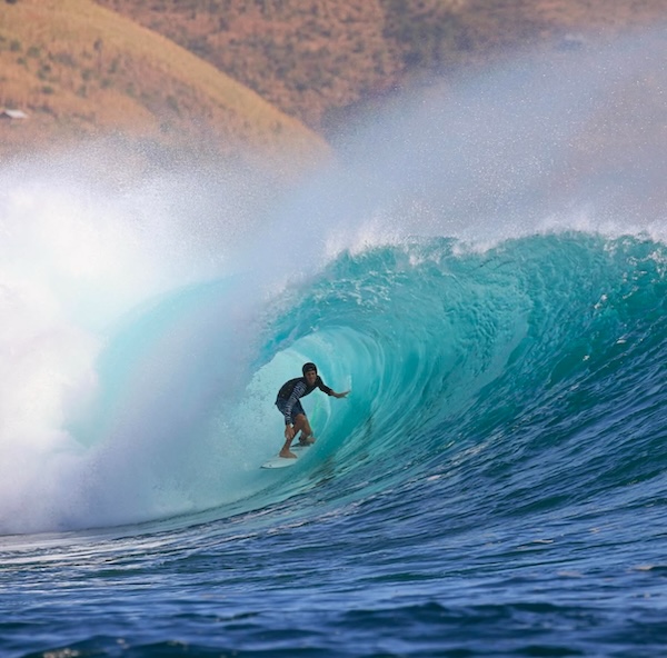 Surfer riding inside a large, turquoise wave.
