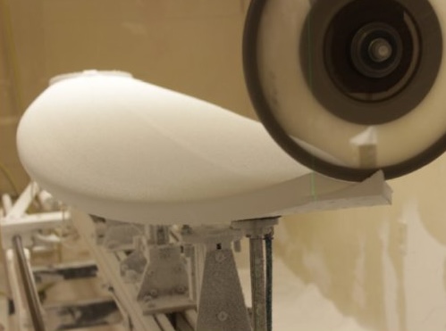 Surfboard being shaped with a sanding tool.