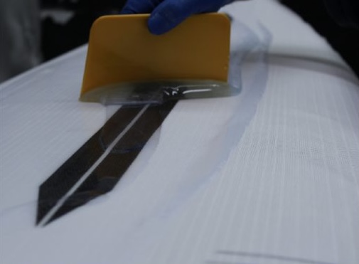 Applying a yellow squeegee to a surfboard's surface.