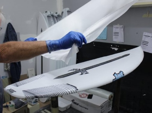 Person applying a protective layer to a surfboard.