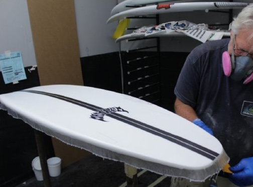 Person shaping a surfboard in a workshop.