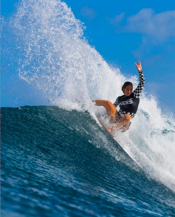 Surfer performing a trick on a wave, hand raised in victory.