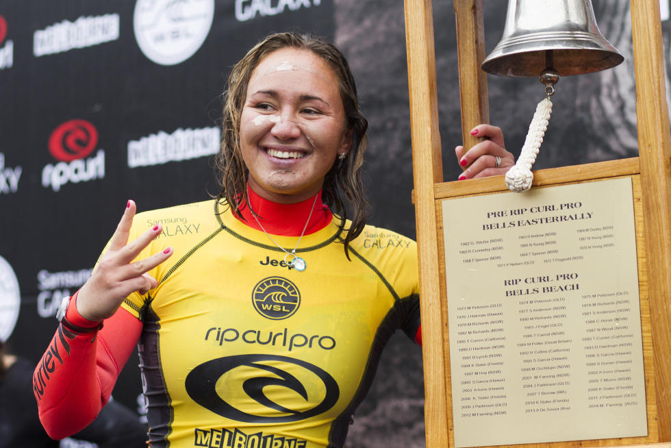 Surfer celebrating victory beside a trophy and bell.