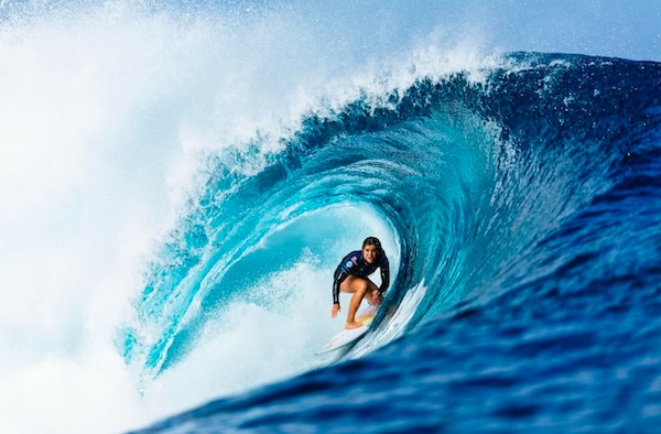 Surfer riding a wave inside a large turquoise barrel.