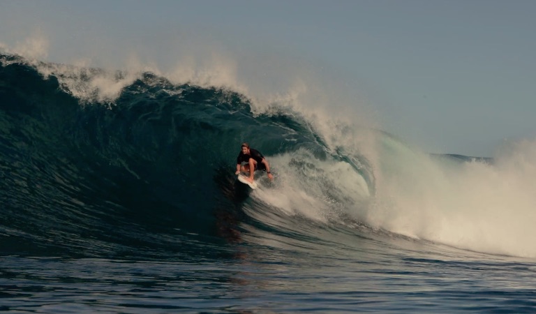 Surfer riding a large wave under a clear blue sky.