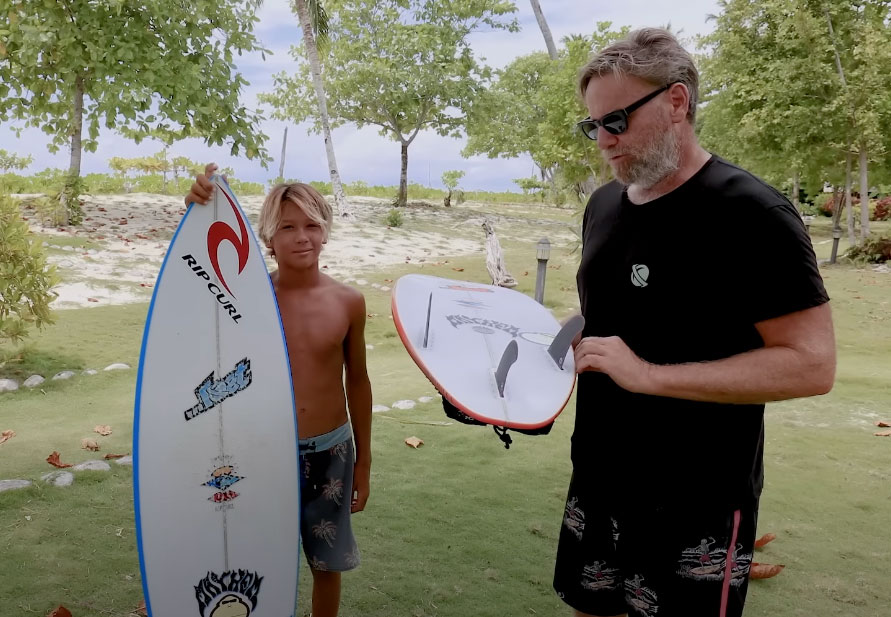 Boy holding a surfboard next to an adult man with another board.