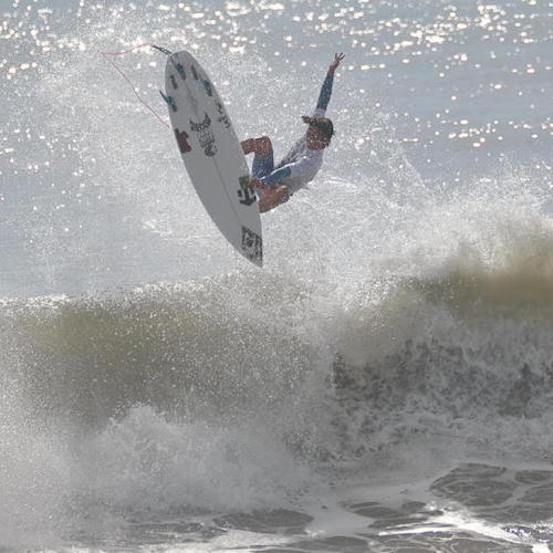 Surfer performing a trick above a large wave.