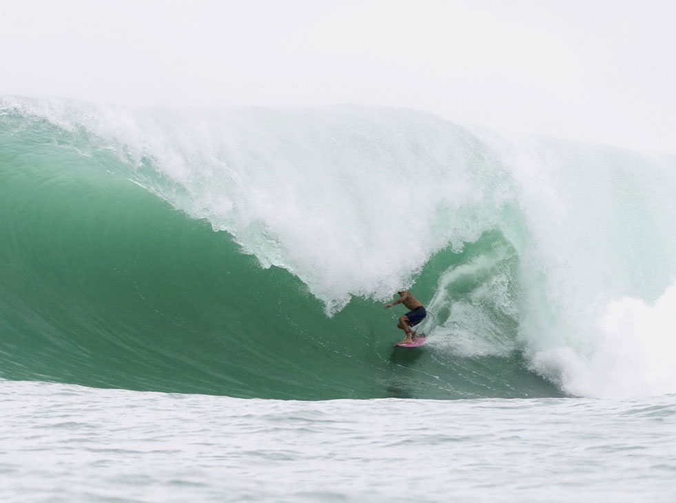 Surfer riding a large green wave in the ocean.
