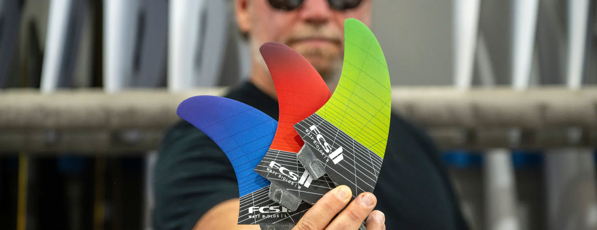 Person holding three colorful surfboard fins in a workshop.