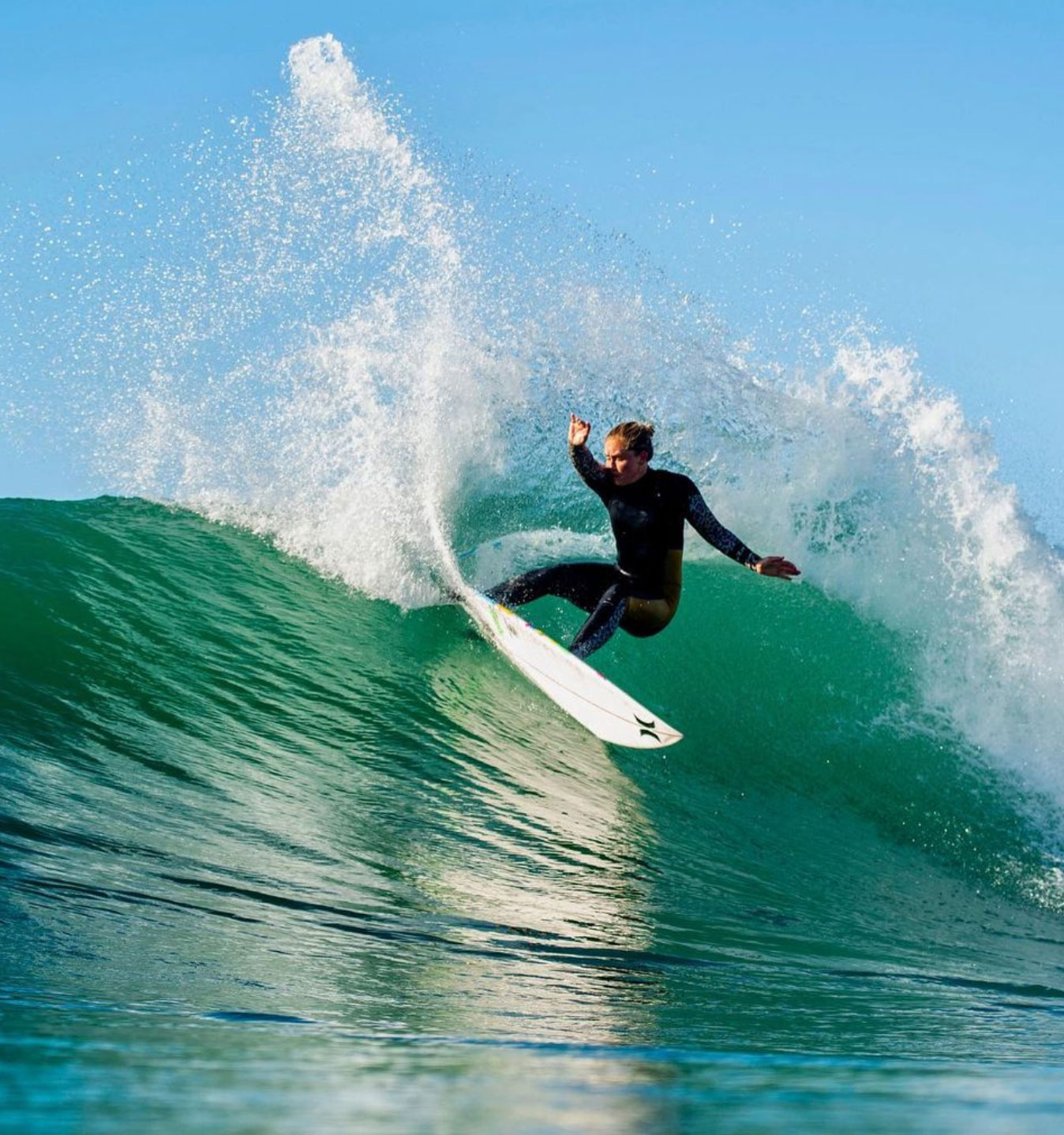 Surfer performing a maneuver on a wave under clear blue sky.