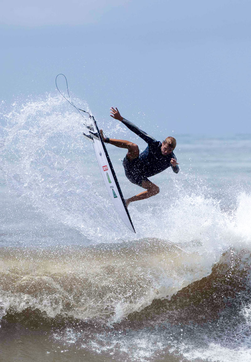 Surfer performing a trick above crashing waves.