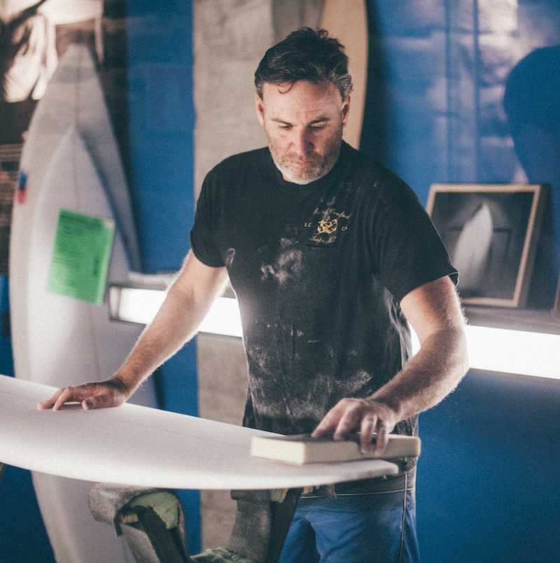 Man shaping a surfboard in a workshop.
