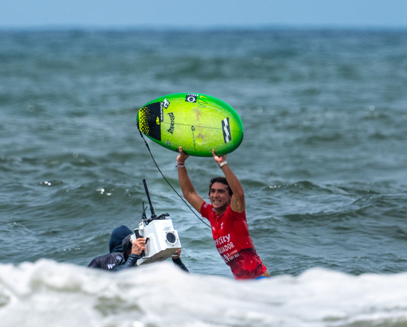 Surfer celebrating with a green board, photographer nearby.