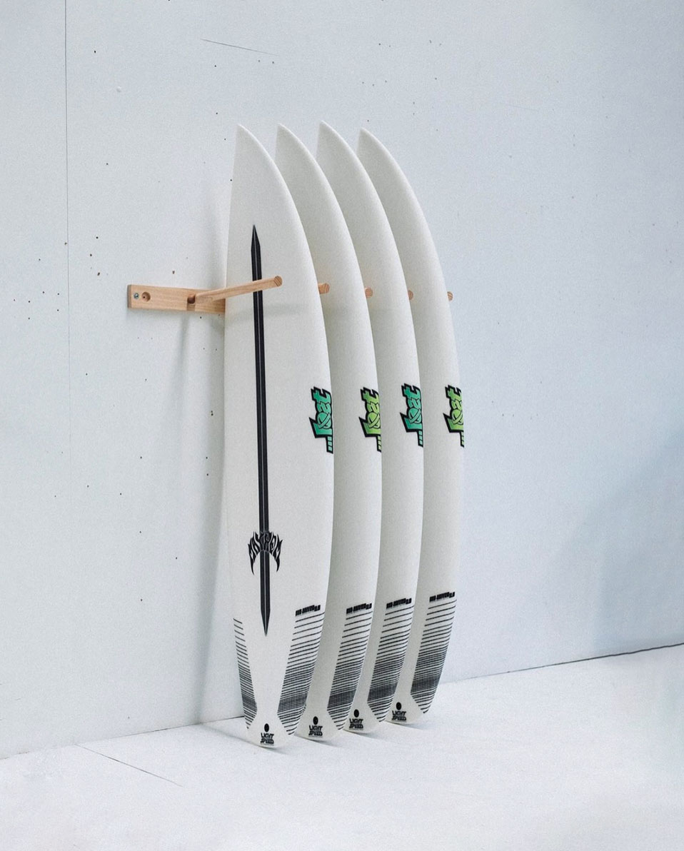 Four surfboards displayed on a wooden rack against a white wall.