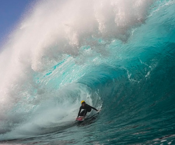 Surfer riding a large wave in vibrant turquoise water.
