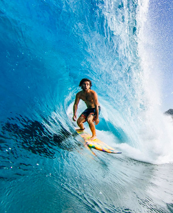 Surfer riding a wave inside a barrel with blue water.