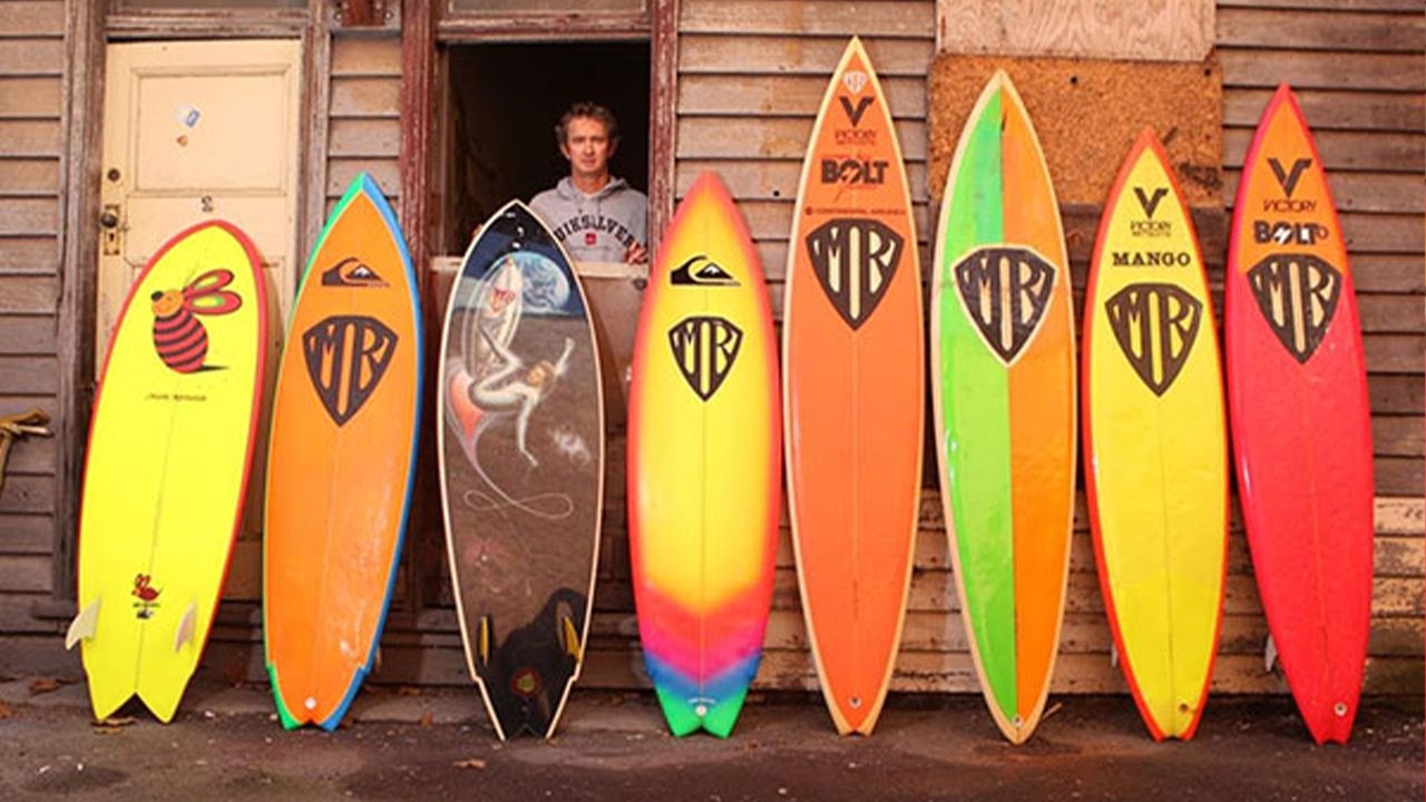 Surfer standing in doorway with colorful surfboards displayed.