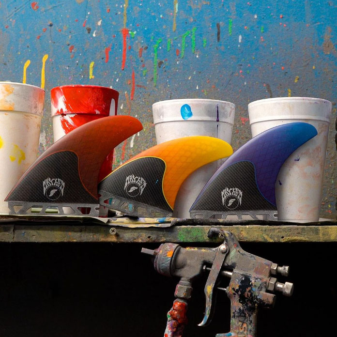Colorful surfboard fins displayed next to paint cups and spray gun.