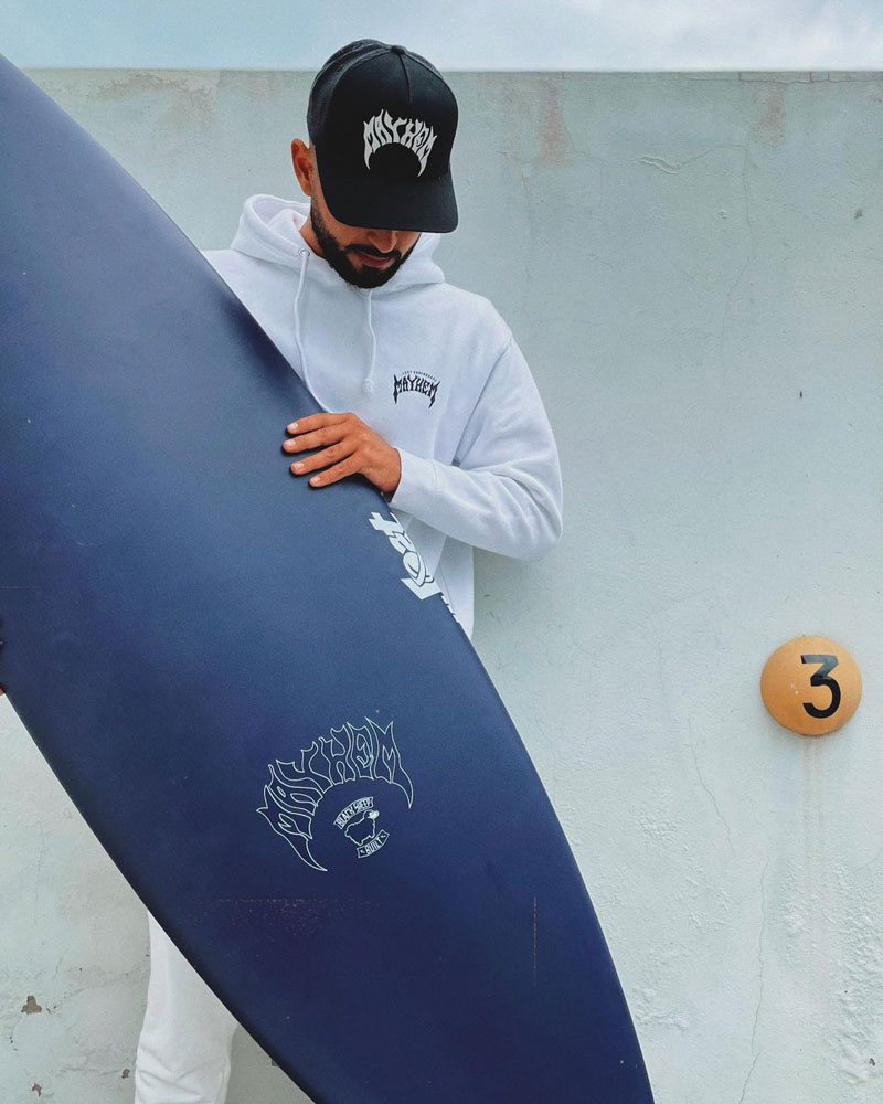 Person in a white hoodie and cap holding a surfboard.