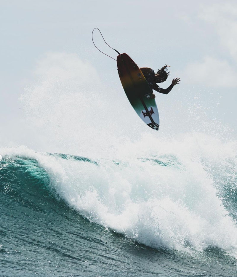 Surfer performing a jump above a large wave.