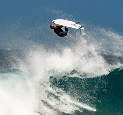 Surfer performing an aerial maneuver above a large wave.