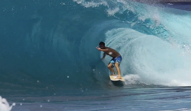 Surfer riding a large wave in clear blue water.