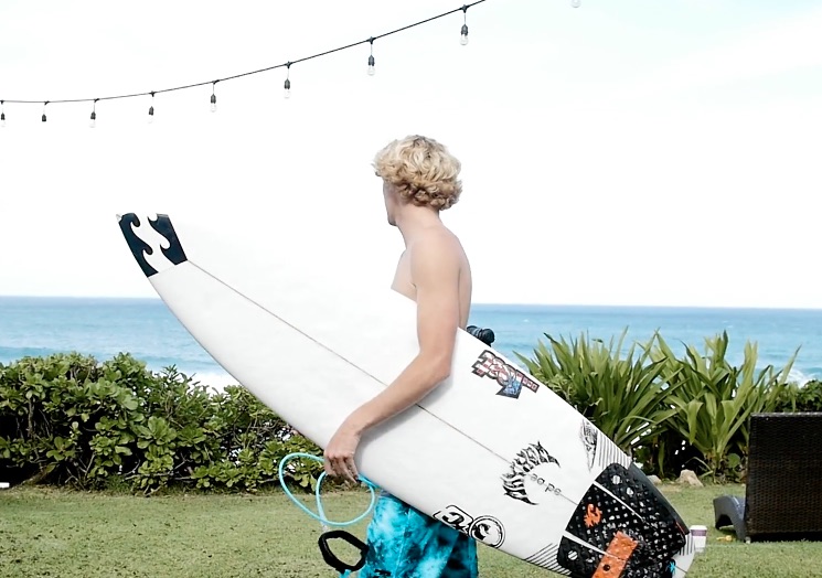 Surfer holding a board, looking towards the ocean.