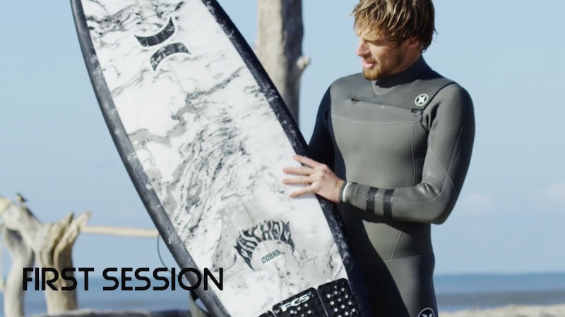 Surfer in wetsuit holding a surfboard on the beach.
