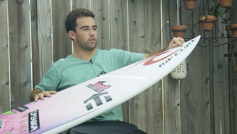 Person sitting with a surfboard in a backyard setting.