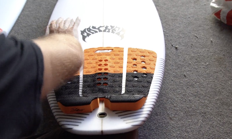 Person applying grip pad to a surfboard on a carpeted surface.