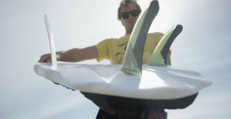 Surfer holding a surfboard with fins against a bright sky.