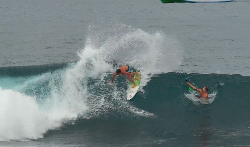 Surfer performing a trick on a wave, another person nearby.