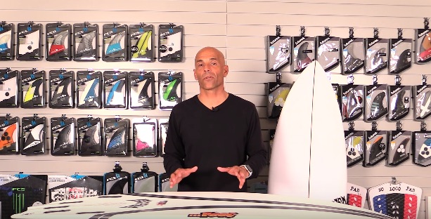 Man standing in front of surfboards and surfboard fins display.