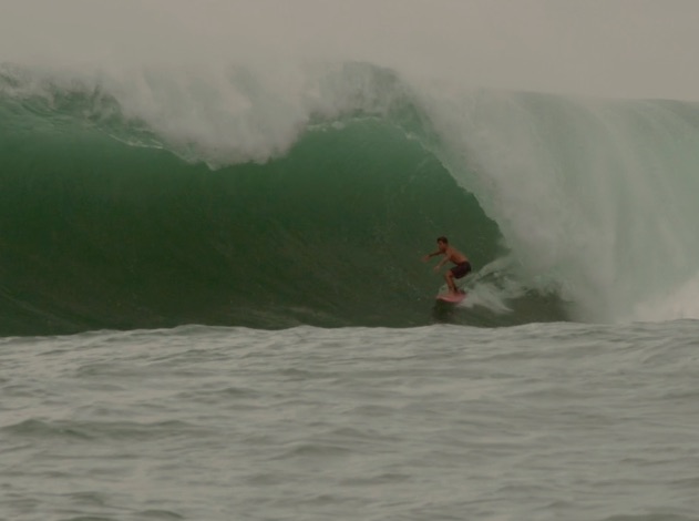 Surfer riding a large green wave in the ocean.