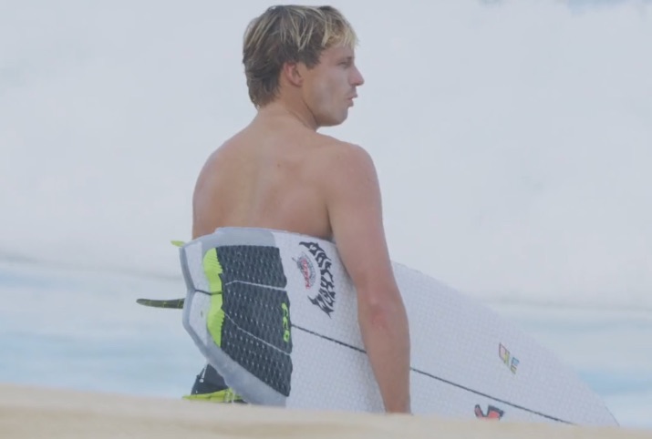 Surfer holding a board, looking towards the ocean.