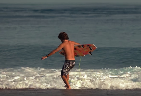 Surfer walking towards the ocean with a surfboard.