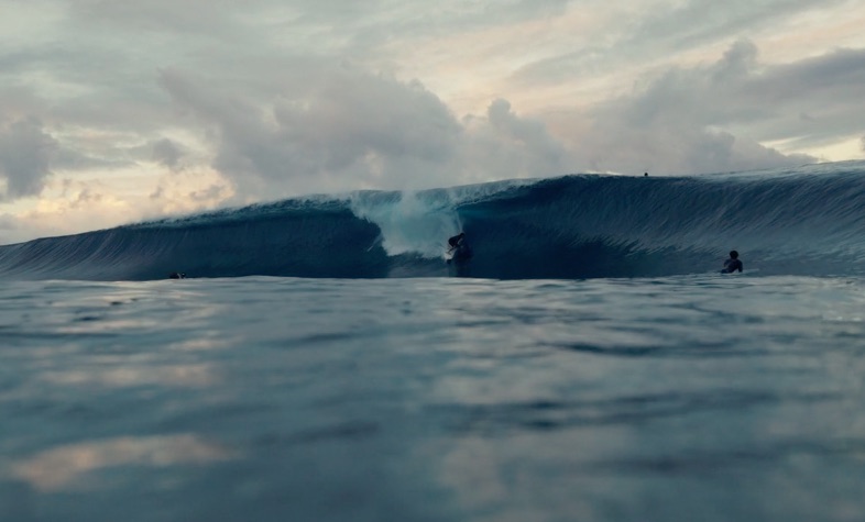 Surfer riding a wave with cloudy sky in the background.