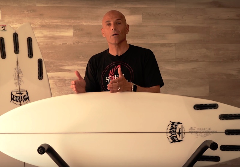 Man explaining surfboard features with surfboards in background.