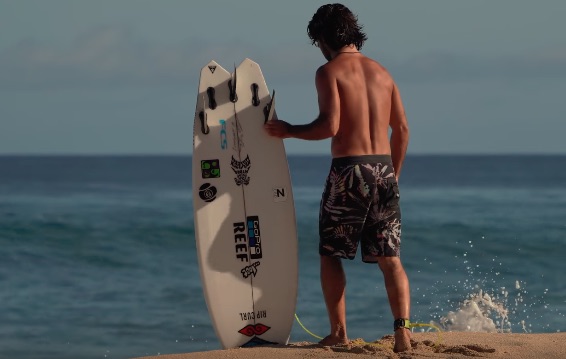 Surfer holding a surfboard on the beach, facing the ocean.