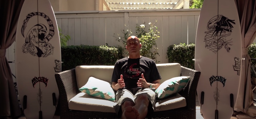 Person sitting on a couch between two surfboards outdoors.