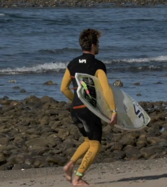 Surfer walking on the beach with a surfboard.