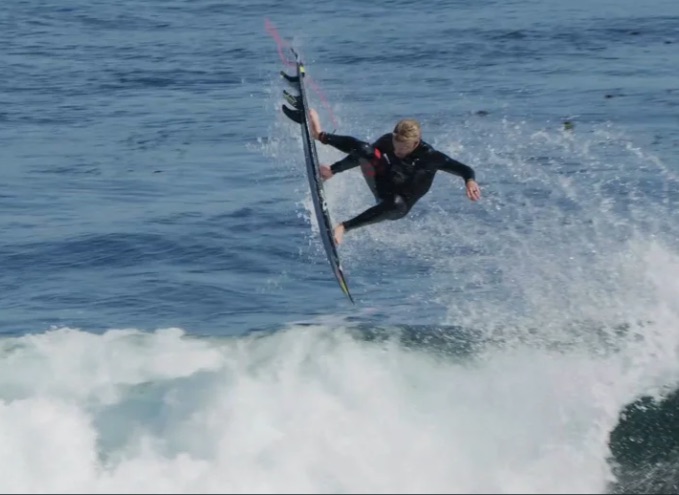 Surfer performing an aerial maneuver above ocean waves.