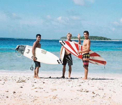 Three surfers standing on a beach with surfboards.