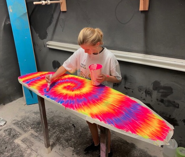 Person painting a colorful swirl design on a surfboard.