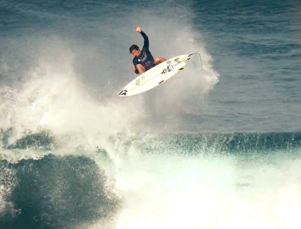 Surfer performing an aerial maneuver above ocean waves.