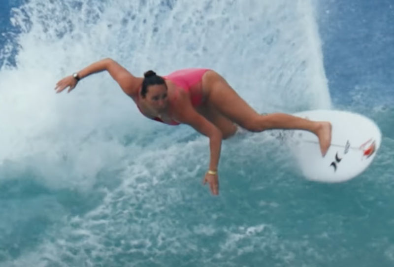 Surfer in pink swimsuit performing a maneuver on a wave.