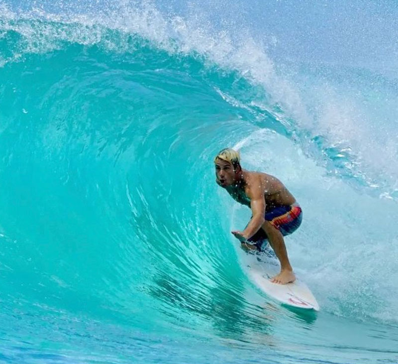 Surfer riding a wave in clear blue water.