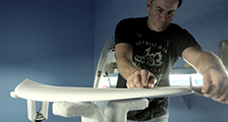 Person shaping a surfboard in a workshop.