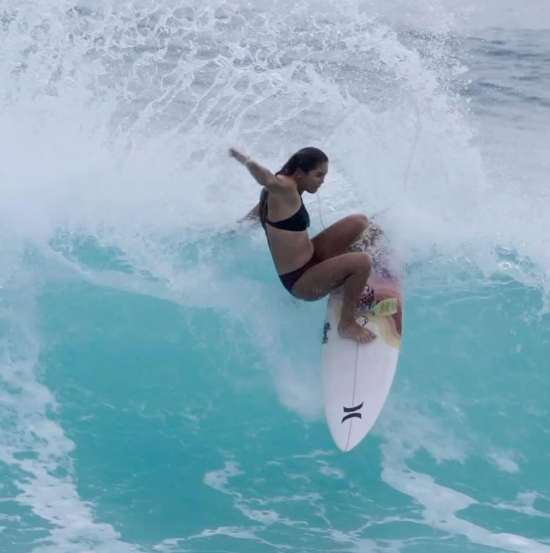 Surfer performing a maneuver on a wave in turquoise water.