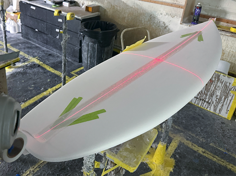Surfboard with laser guide in a workshop setting.